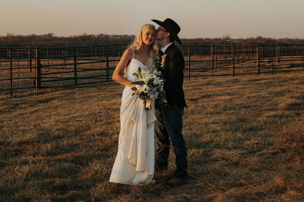 Western-themed sunset wedding portrait with couple embracing in front of rustic ranch fencing at golden hour.