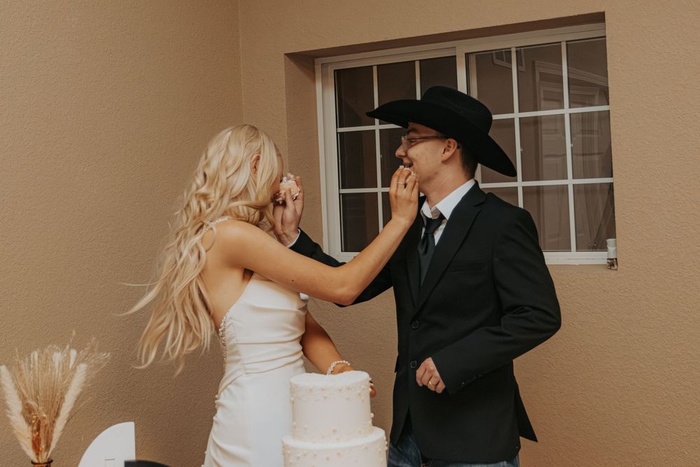 Wedding couple sharing playful cake-smearing moment during their reception celebration.