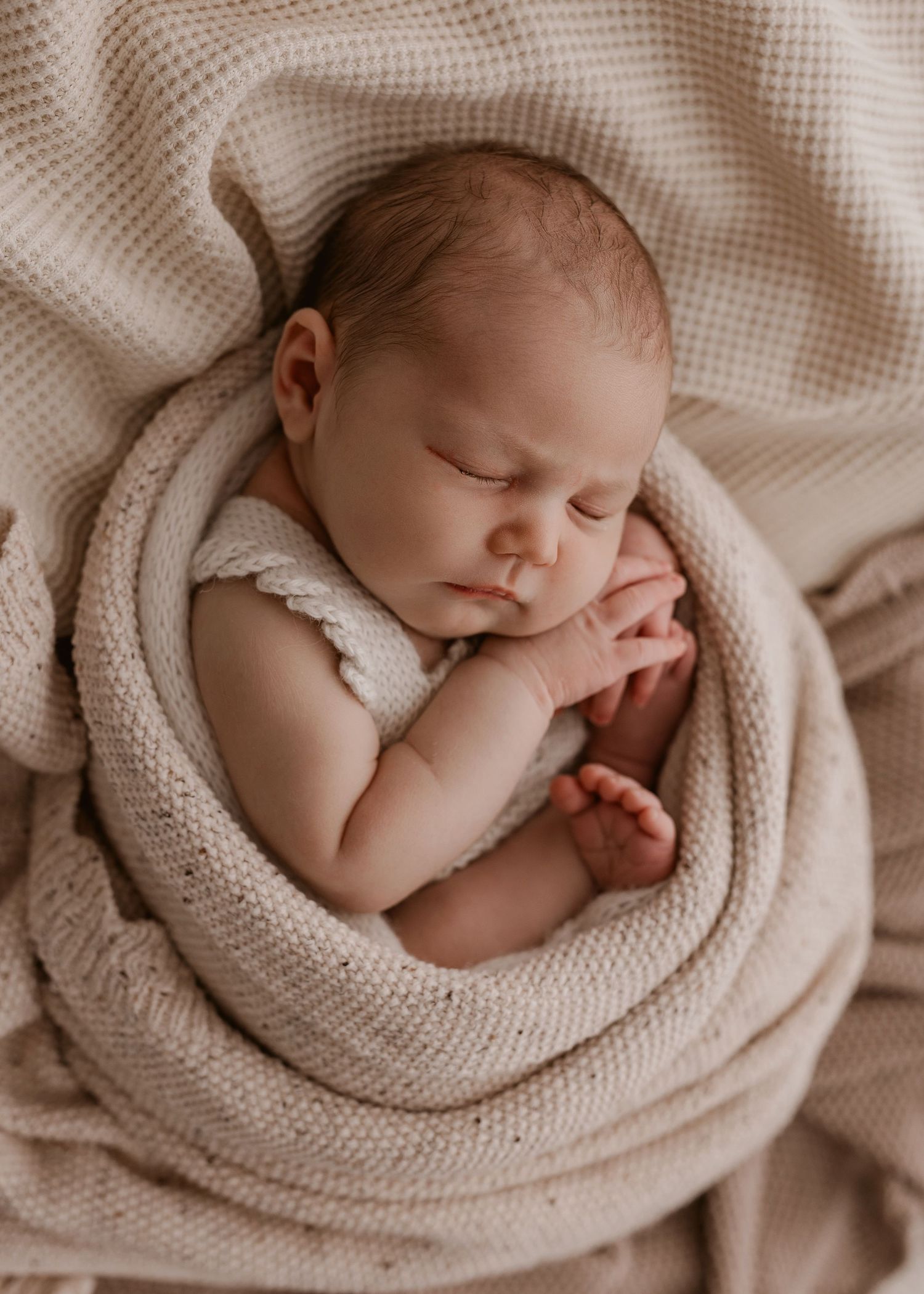 Sweet newborn baby sleeping peacefully wrapped in cozy beige knit blanket in soft natural light.