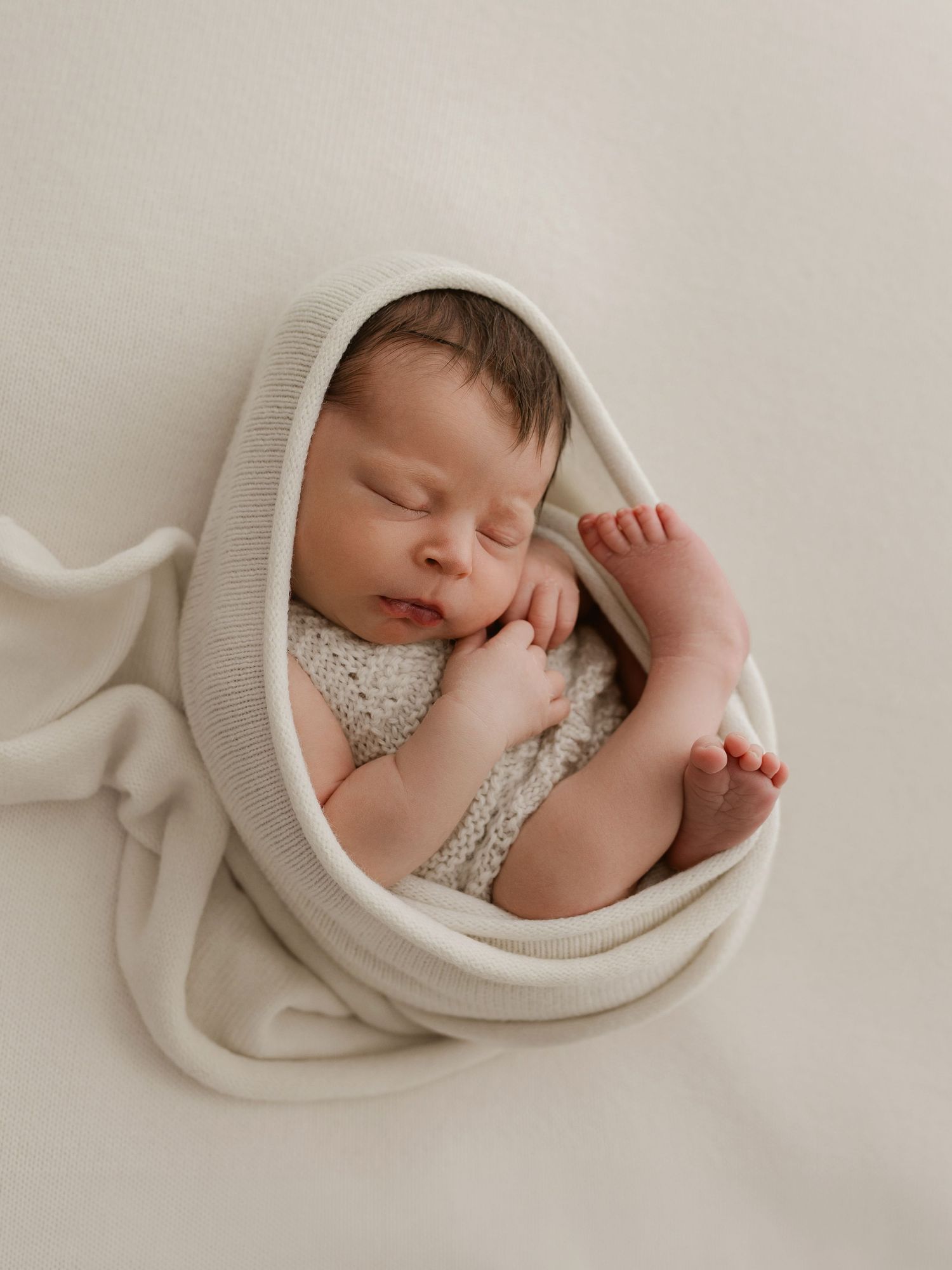 Sweet newborn baby sleeping peacefully wrapped in cozy beige knit blanket in soft natural light.