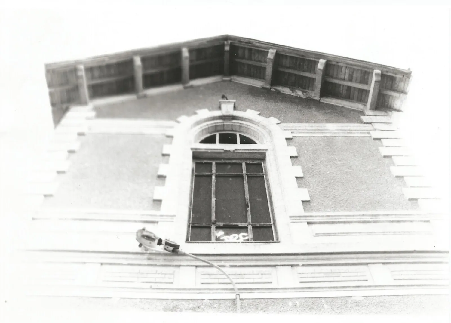 Vue en contre-plongée d’une maison avec un toit en triangle et une fenêtre centrale, prise en noir et blanc avec lumière intense.