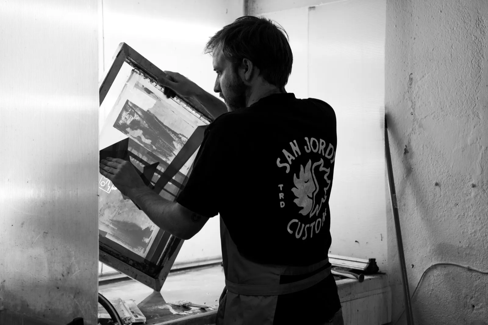 Artisan manipulant un cadre de sérigraphie en atelier, éclairage tamisé.