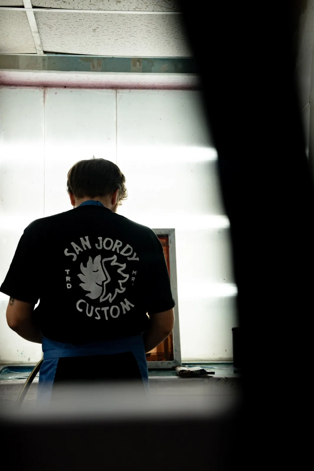 Dos d’un artisan en atelier, assis devant une source de lumière en attente de tirage.