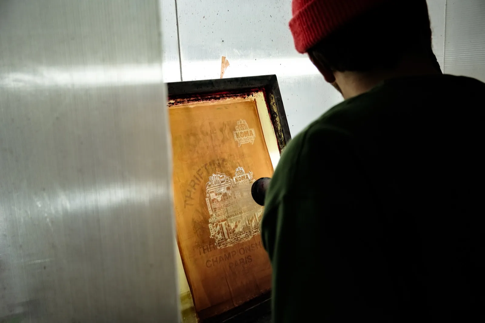 Personne en bonnet rouge inspectant un écran de sérigraphie à contre-jour.