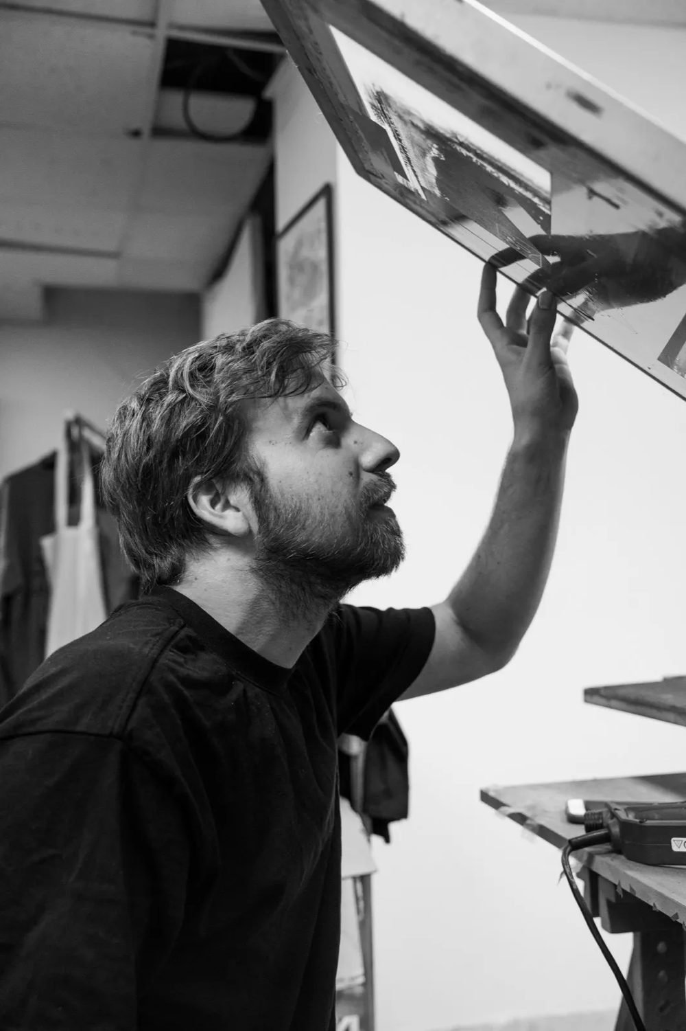 Artisan observant un écran de sérigraphie tenu au-dessus de sa tête.