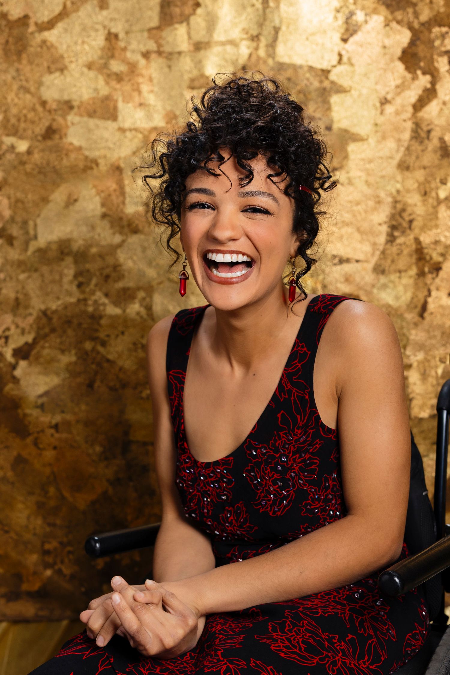 Joyful portrait against textured gold wall wearing red and black sequined dress.