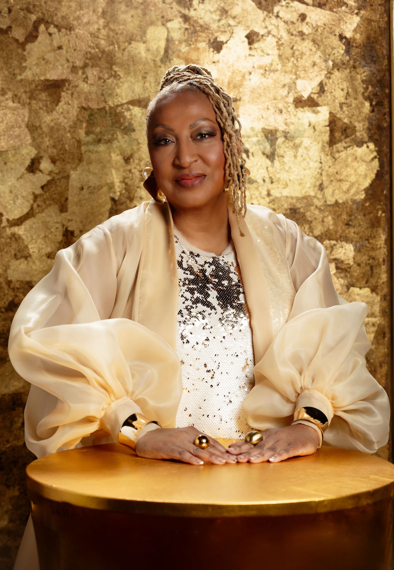 Elegant portrait against a gold metallic backdrop featuring a cream silk blouse and ornate headpiece.