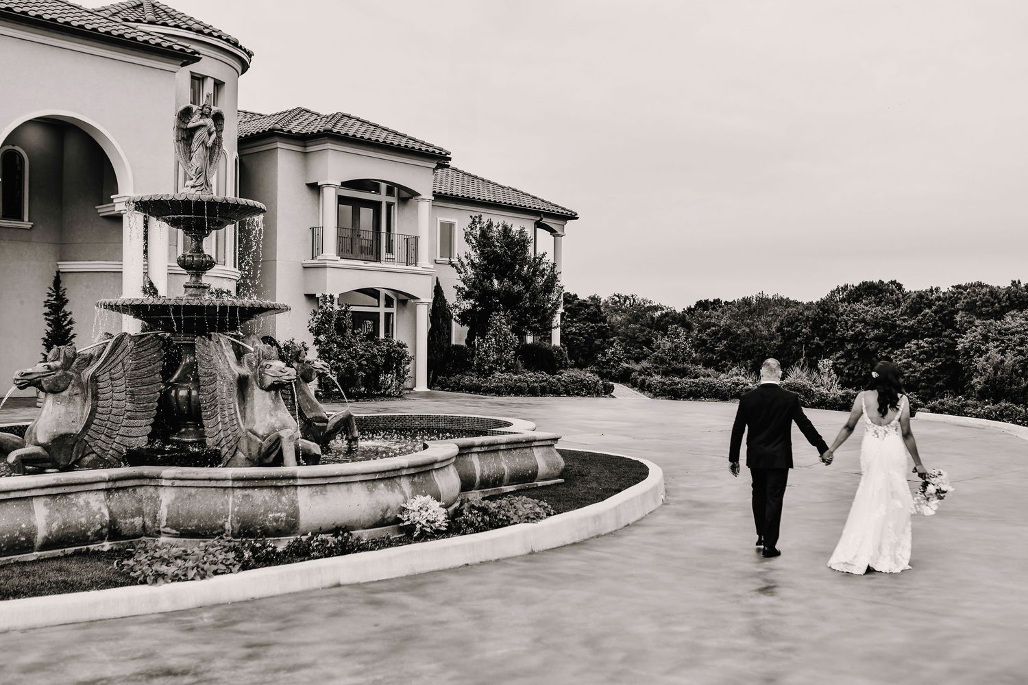 black and white photo of bride and groom holding hands as they walk towards their wedding reception after their wedding ceremony