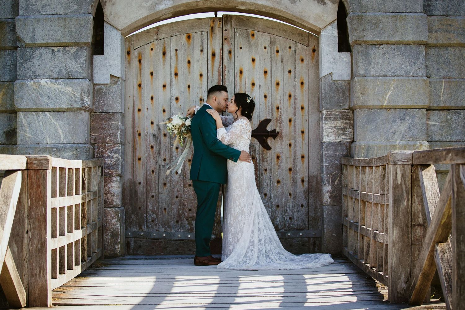 A couple shares a romantic moment in front of an ornate wooden door at a stone castle entrance.