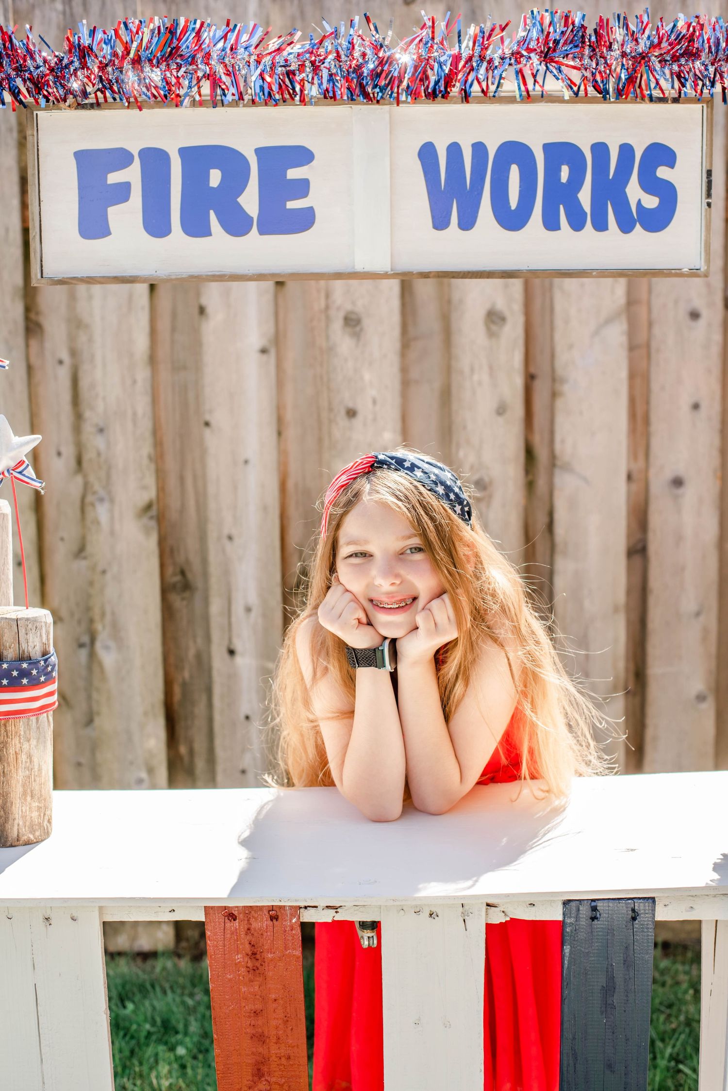 Red white and blue decorated fireworks stand with festive tinsel garland.