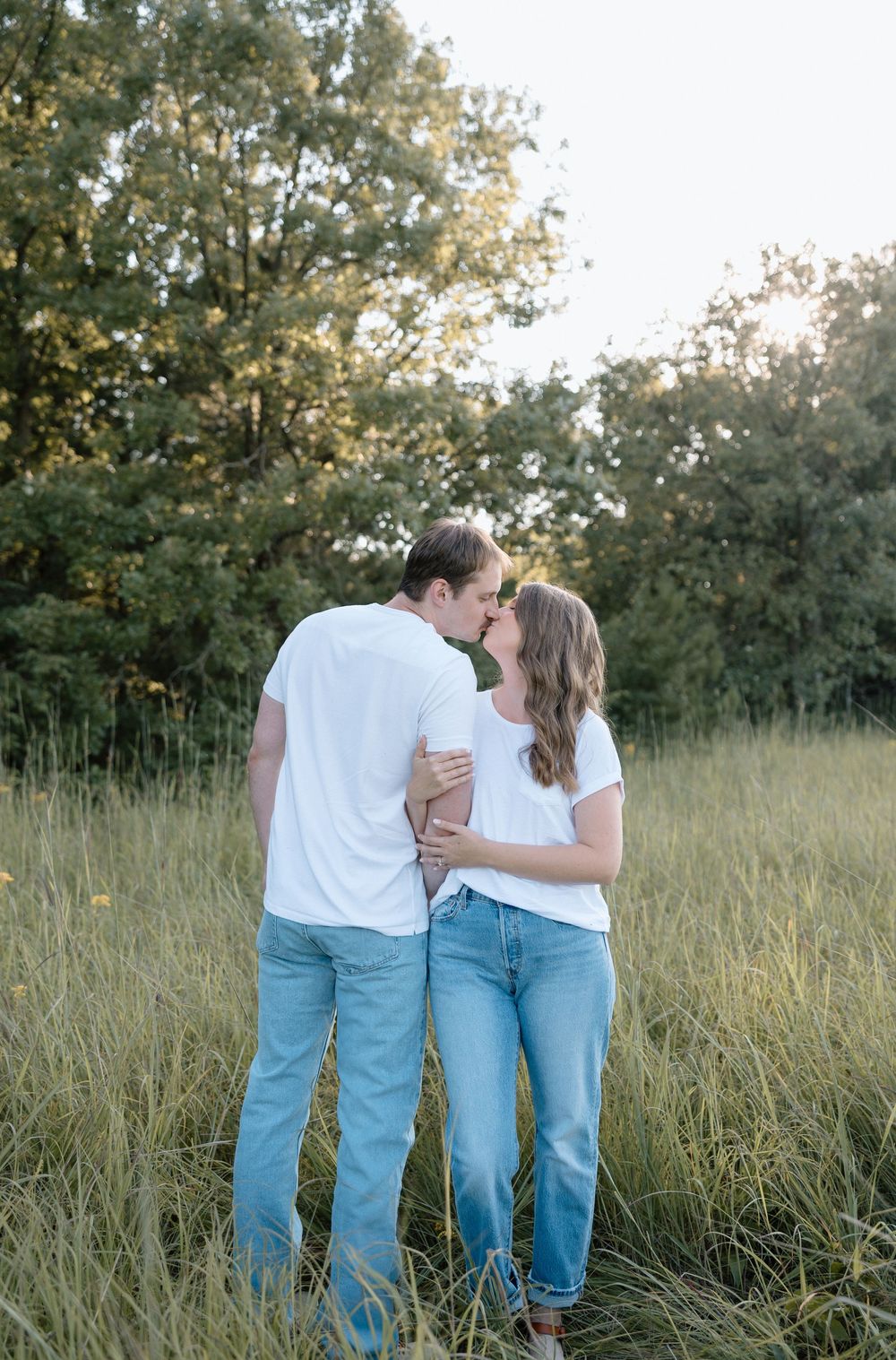 Couple sharing intimate moment in tall grass field during golden hour.