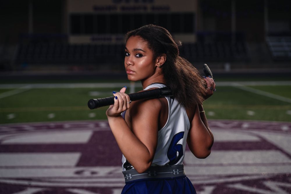 Athlete holding a baseball bat stands ready in batting stance on sports field at dusk.