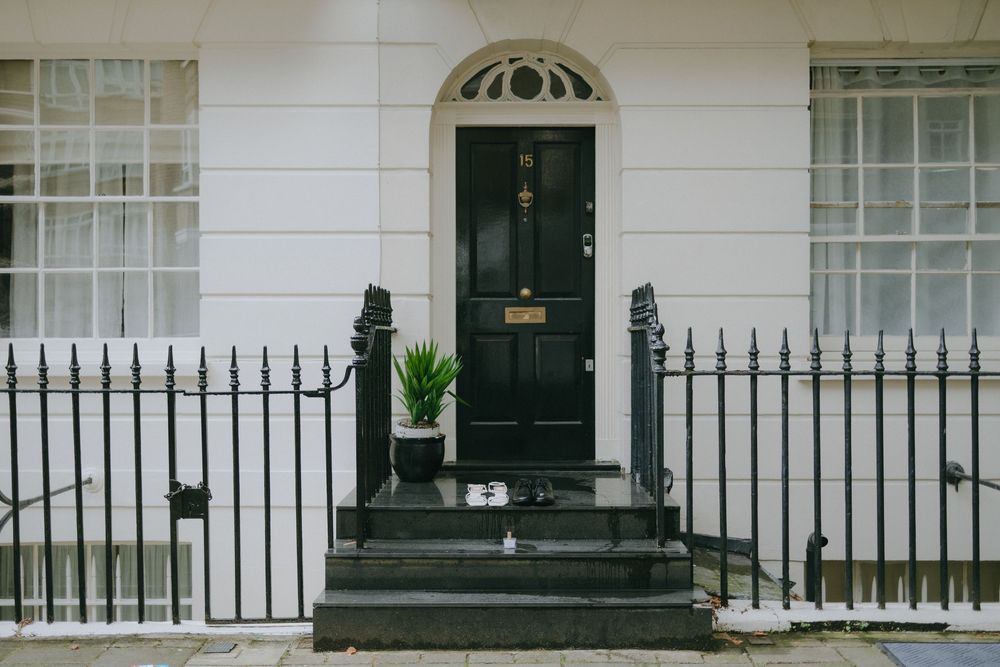 An elegant black door with brass hardware stands between white columns at a London townhouse entrance.