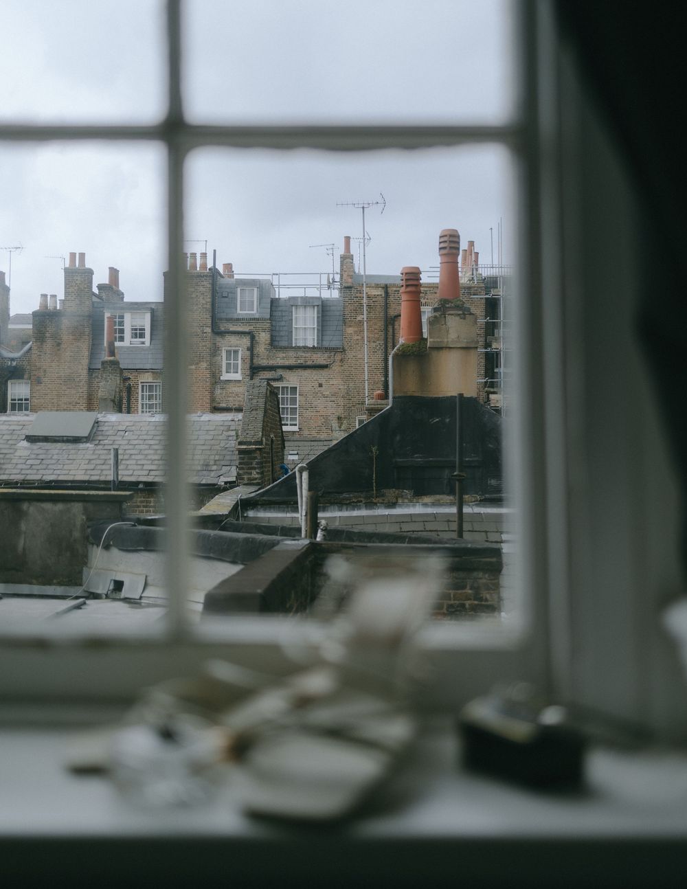 View of old brick chimneys and rooftops through a window on an overcast day.