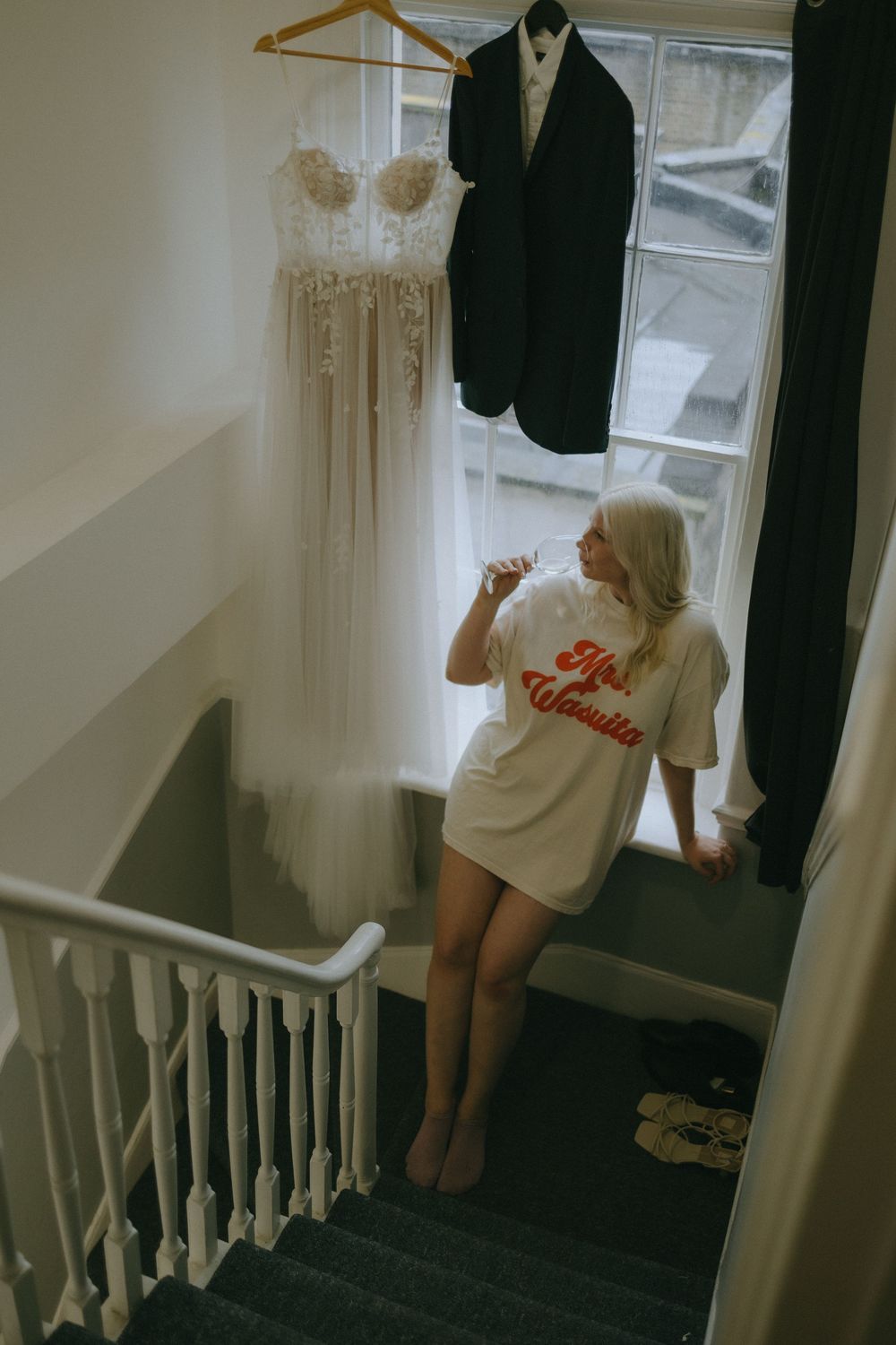 Wedding attire hanging near a stairwell as someone views the dress and suit.