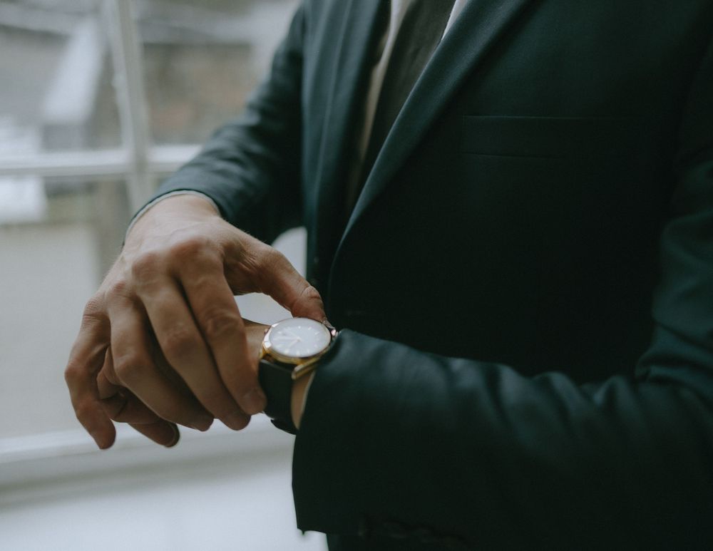 Close-up of hands in a green jacket checking a wristwatch.