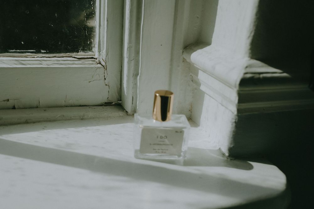 A glass perfume bottle sits on a white windowsill in soft natural light.
