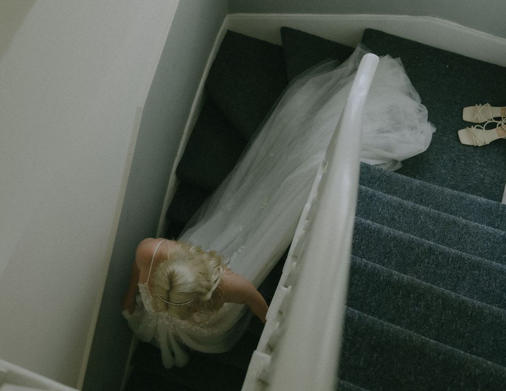 A flowing white wedding dress and veil cascading down dark carpeted stairs.