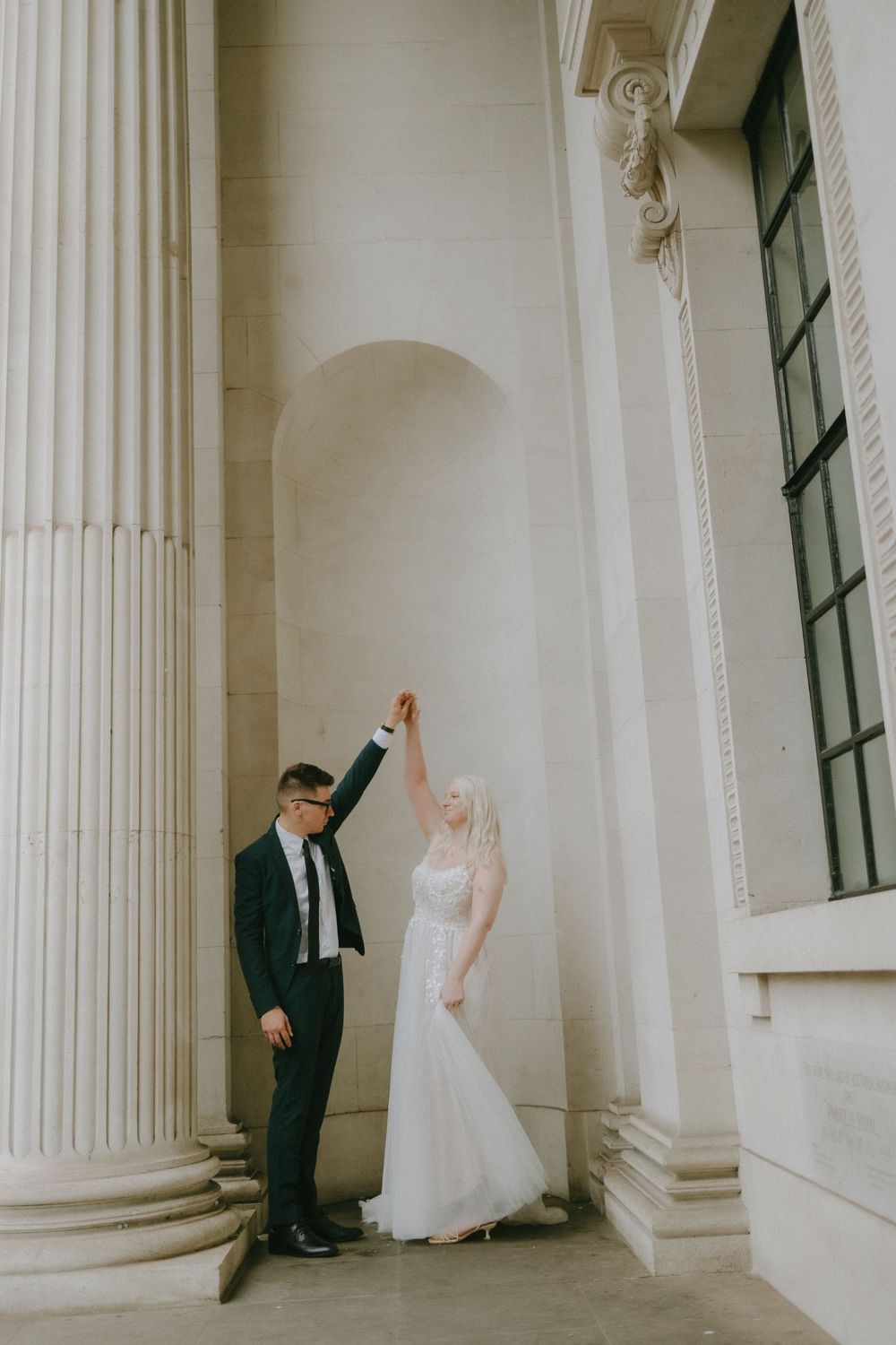 Elegant wedding couple poses between classic white columns with beautiful architectural details.