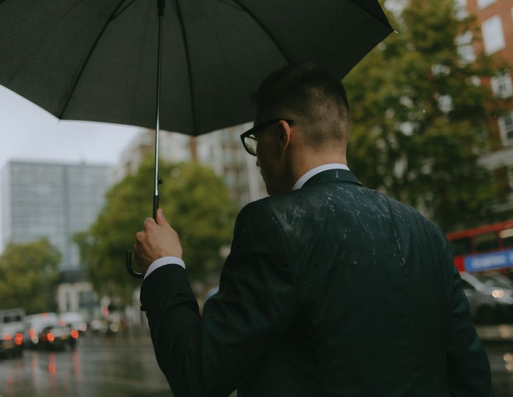 Person in suit holding black umbrella on rainy city street.