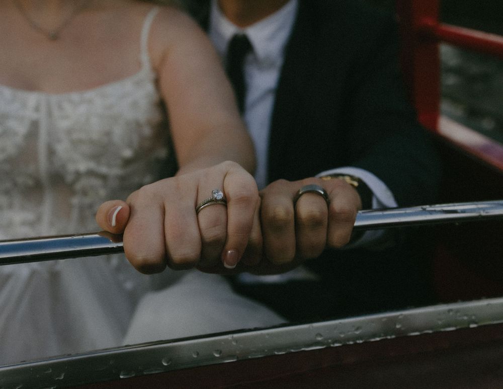 Two hands with wedding rings hold onto a black metal railing in an intimate close-up shot.