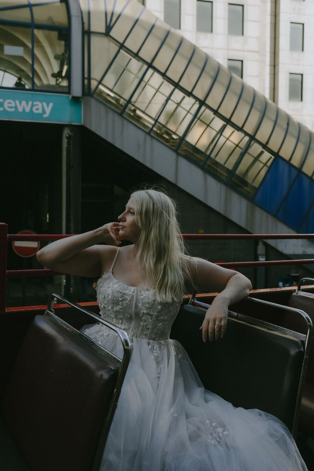 A bride in a white dress poses inside a vintage bus near a Raceway station entrance.