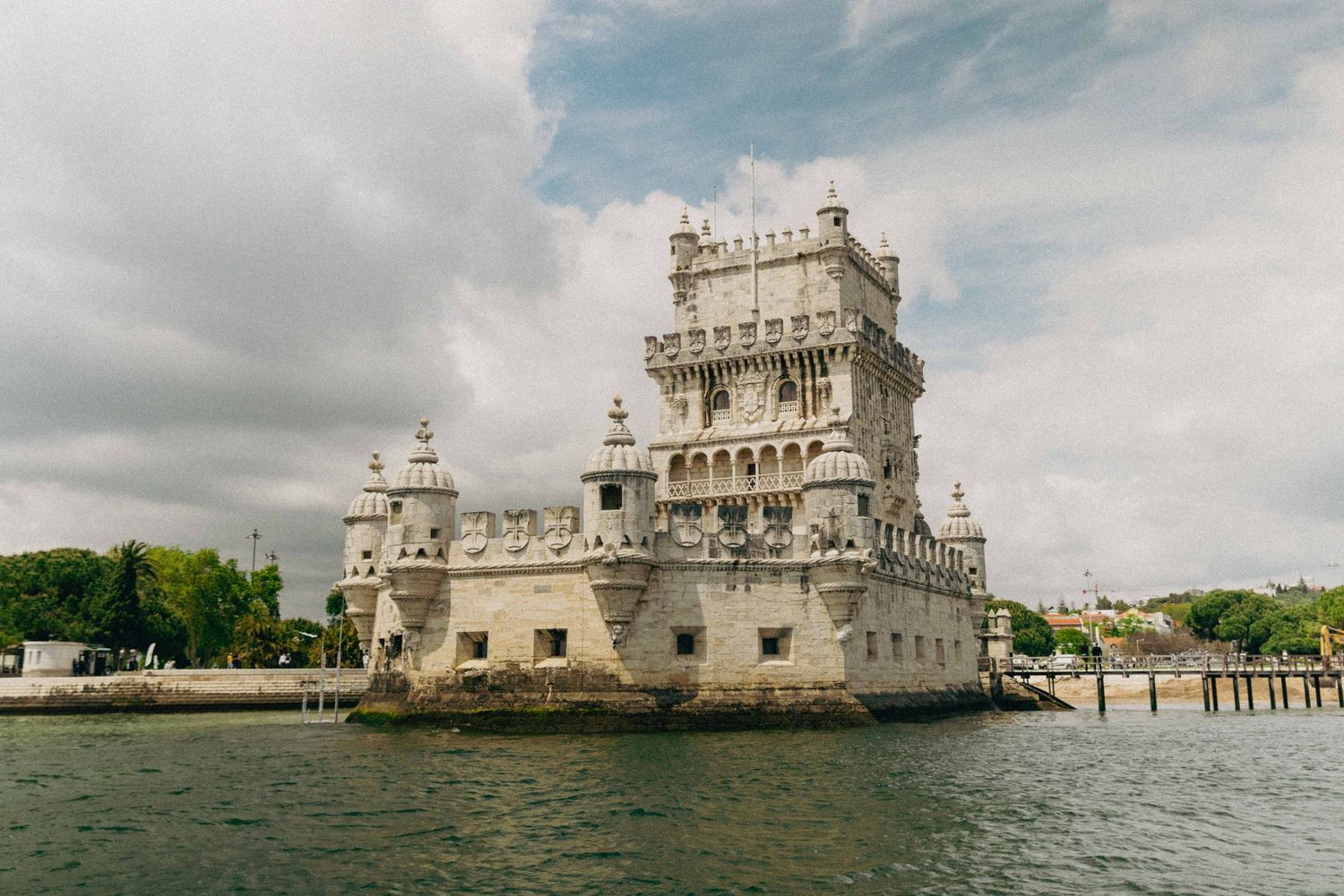 The historic Belem Tower stands majestically on the Tagus River in Lisbon, Portugal under cloudy skies.