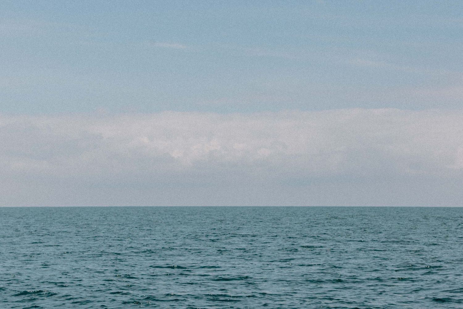A serene seascape with calm blue-green waters meeting the horizon under a pastel sky with soft clouds.