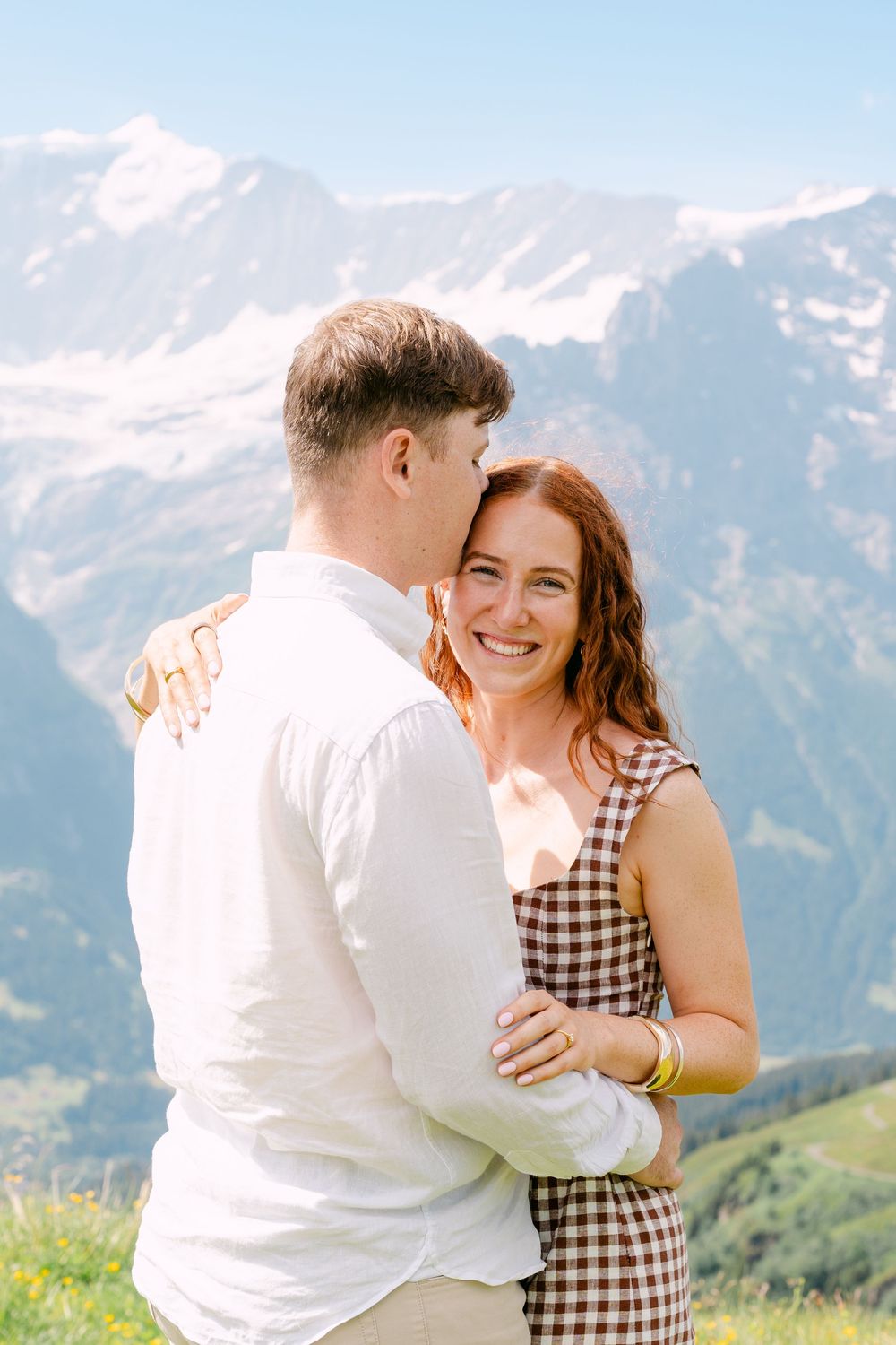 Happy couple embracing with stunning snow-capped mountain backdrop on a sunny day outdoors.