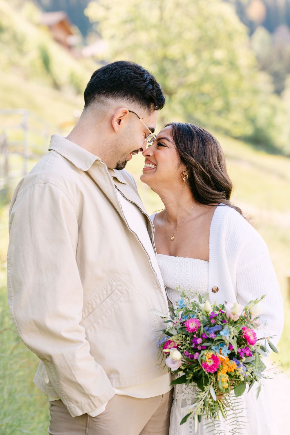 Couple in beige and white attire sharing a romantic moment outdoors, bride holding a colorful wildflower bouquet.