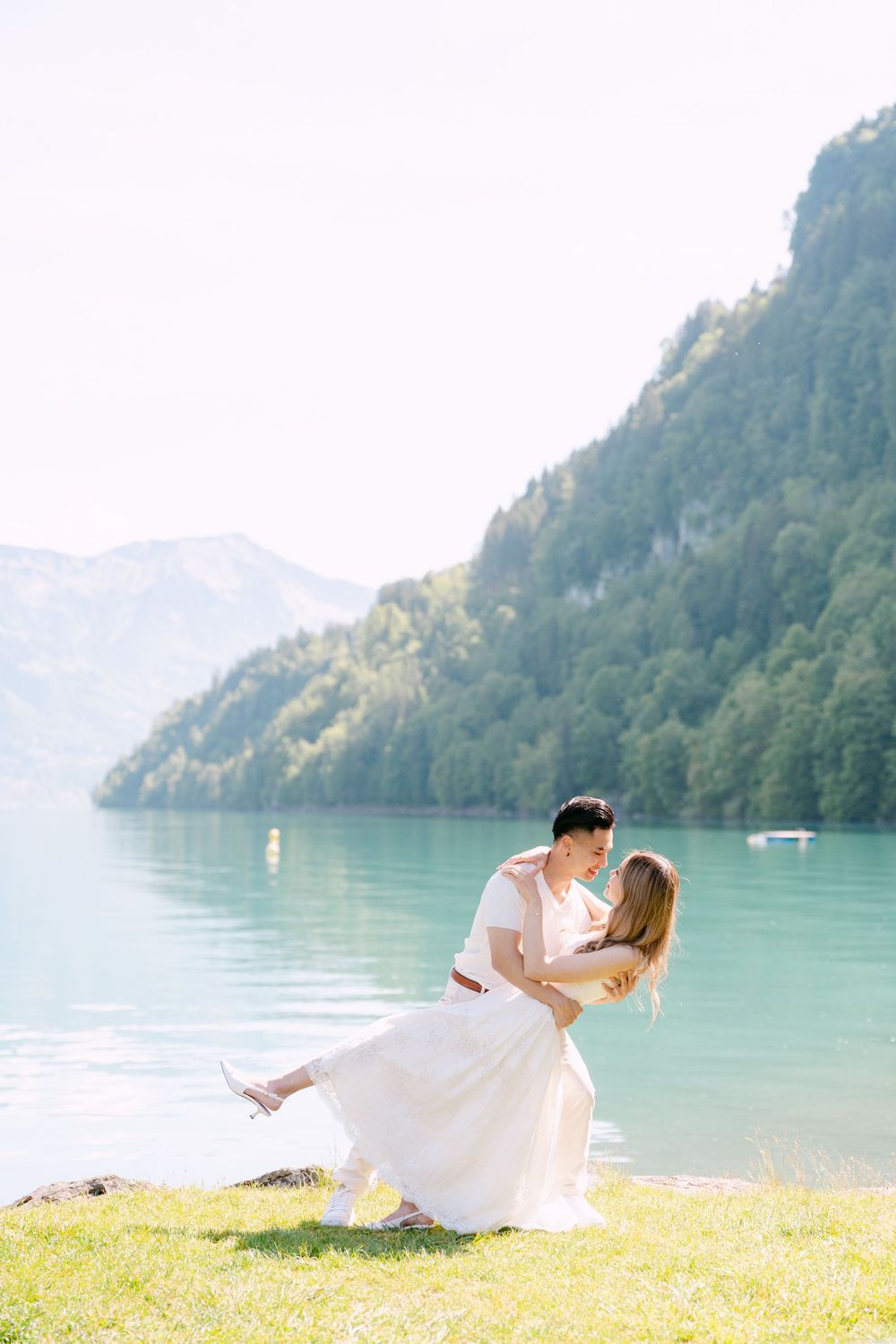 Couple dancing romantically by a turquoise alpine lake with mountain backdrop on a sunny day.