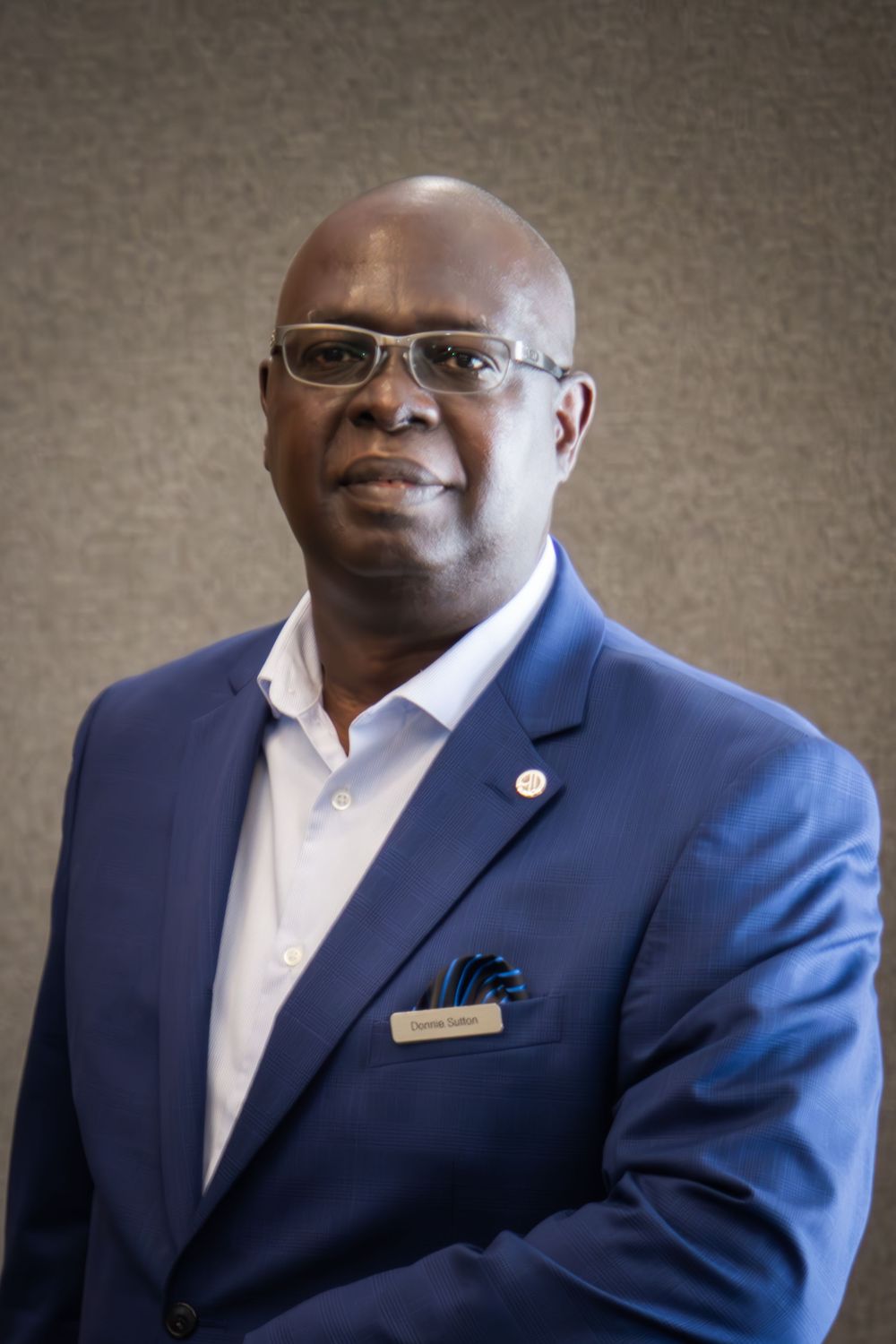 Professional man in blue blazer and glasses poses for formal portrait photo.