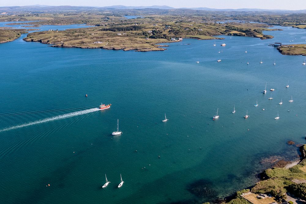 Aerial view of a scenic coastal landscape with sailboats dotting the blue waters near rocky shorelines.