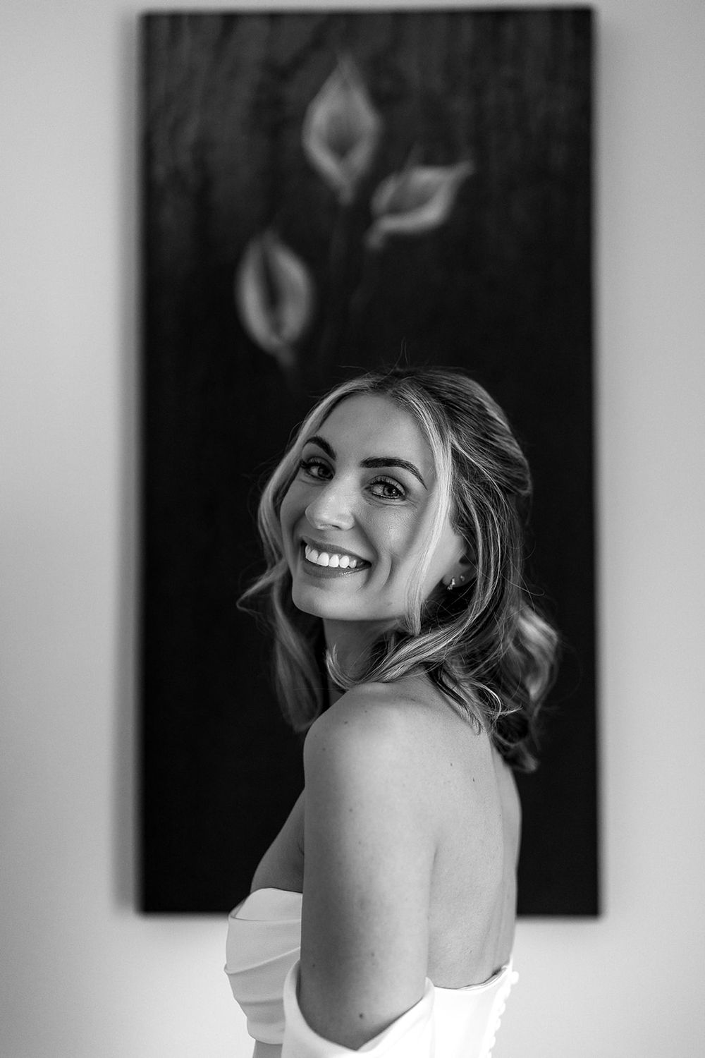 An elegant portrait in black and white showing a radiant smile against an artistic wall backdrop.
