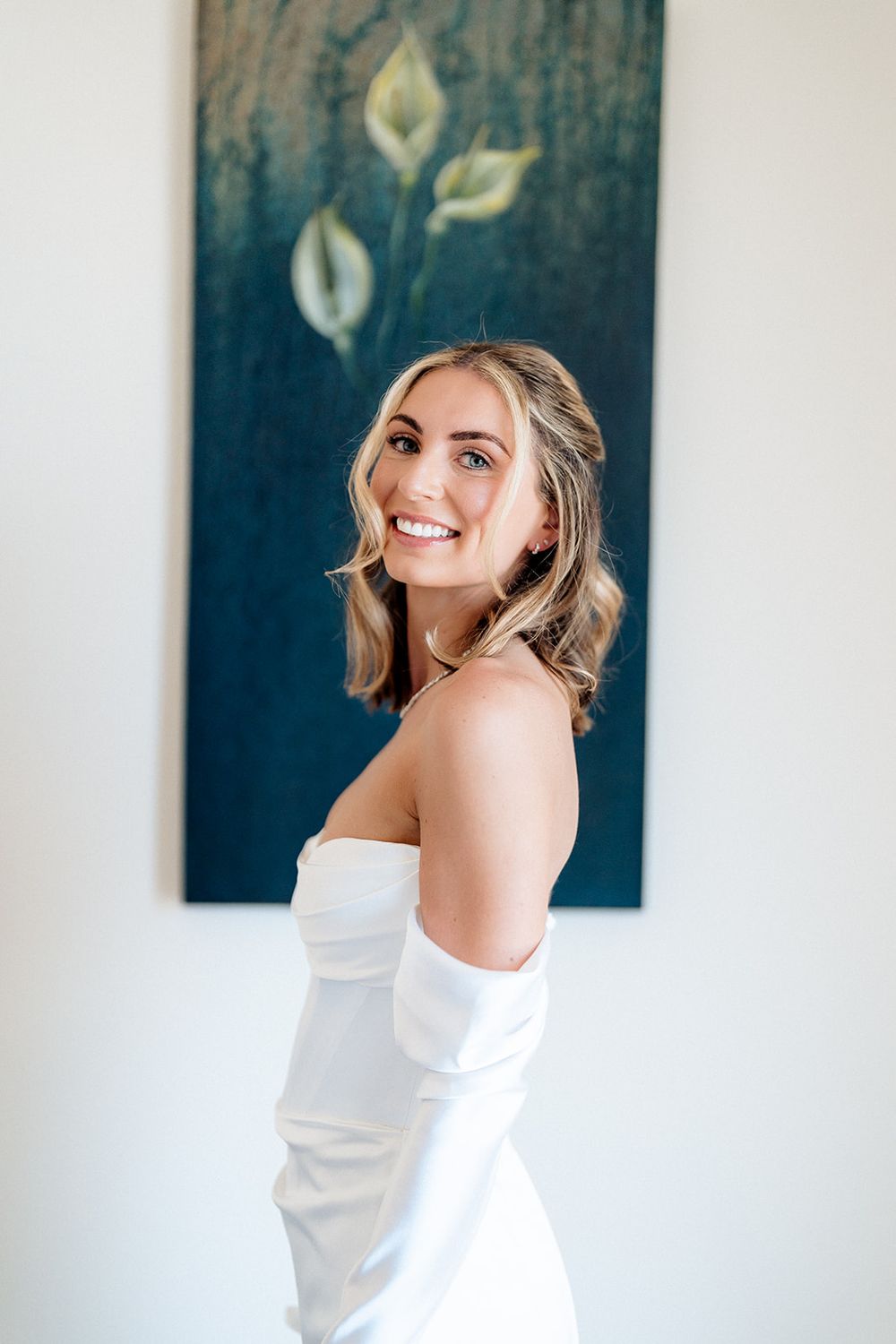 A stunning portrait with a white off-shoulder dress against a blue wall with floral art.