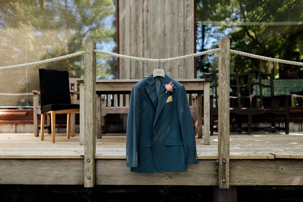 A navy blue suit jacket hanging on a wooden porch railing outdoors against a blurred natural background.