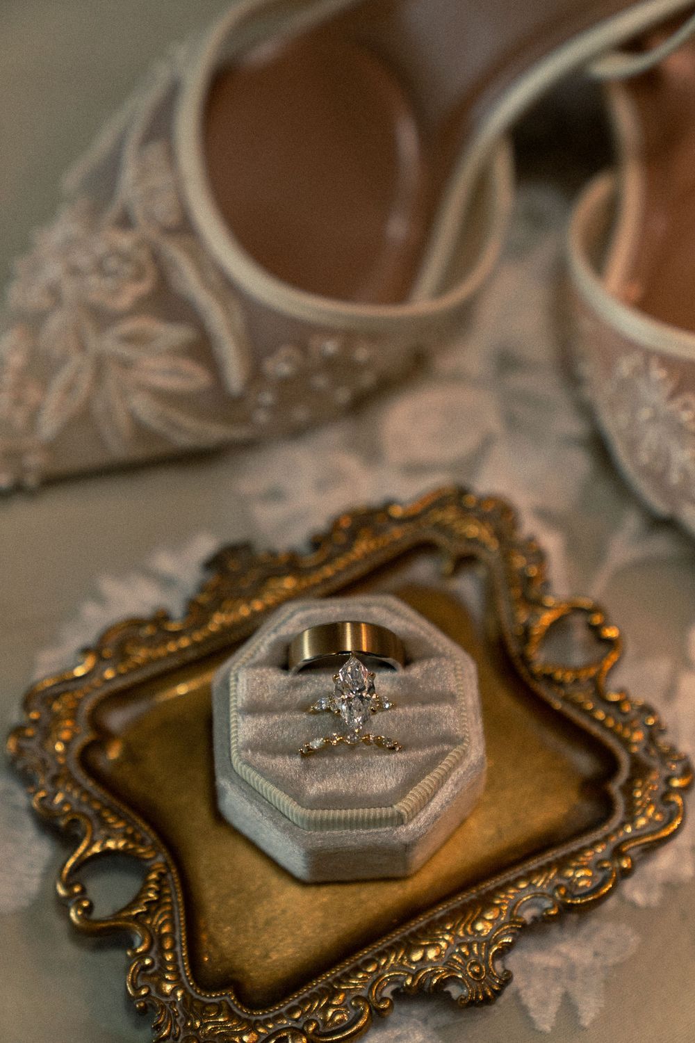 Vintage gold ornate tray with engagement ring displayed on gray velvet cushion in elegant wedding detail shot.
