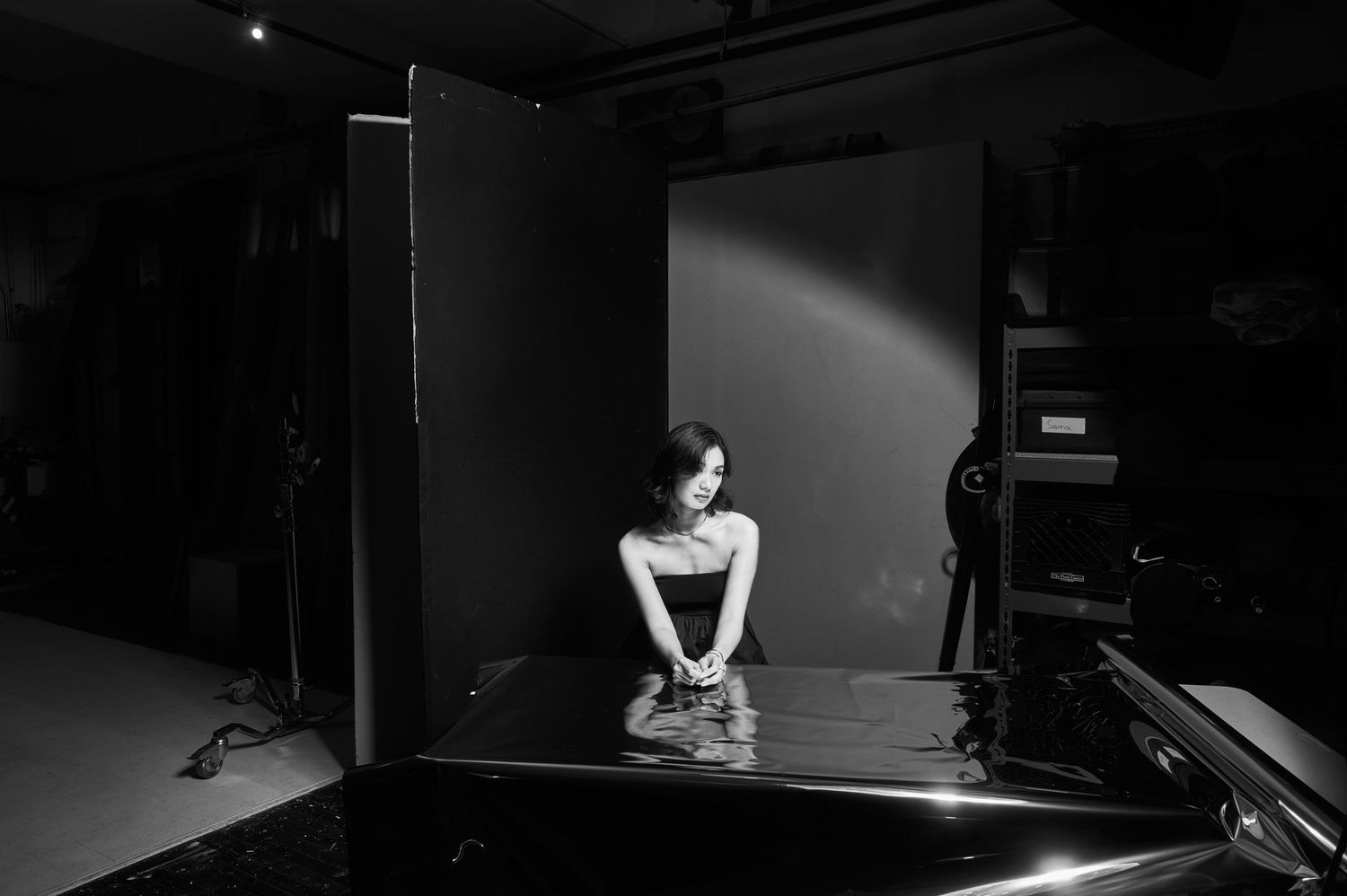 Dramatic black and white studio shot of a dancer seated on stage under a spotlight, creating a moody atmosphere.