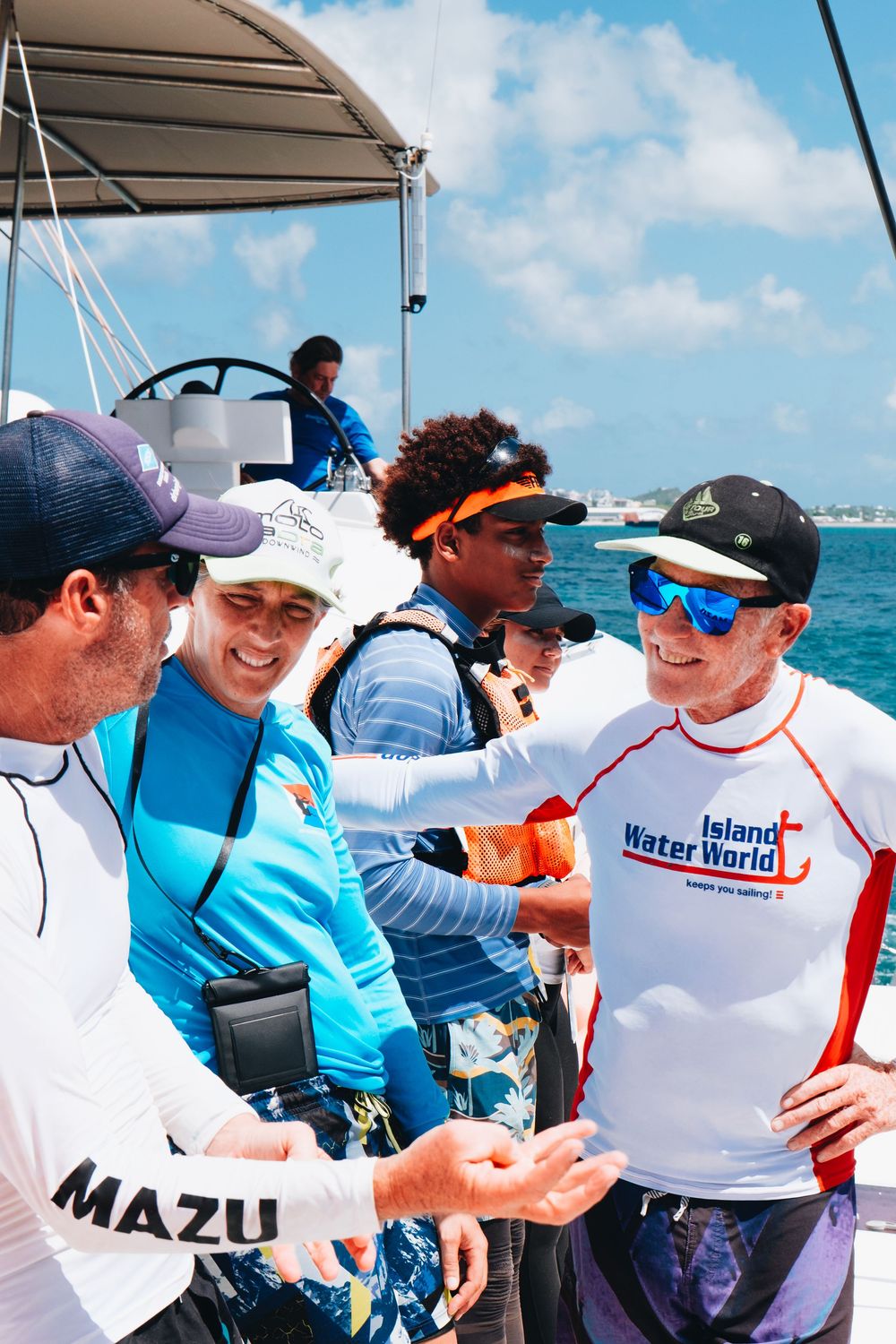 A group gathers on a boat deck during a sunny day on turquoise waters wearing sun protection gear and sportswear.
