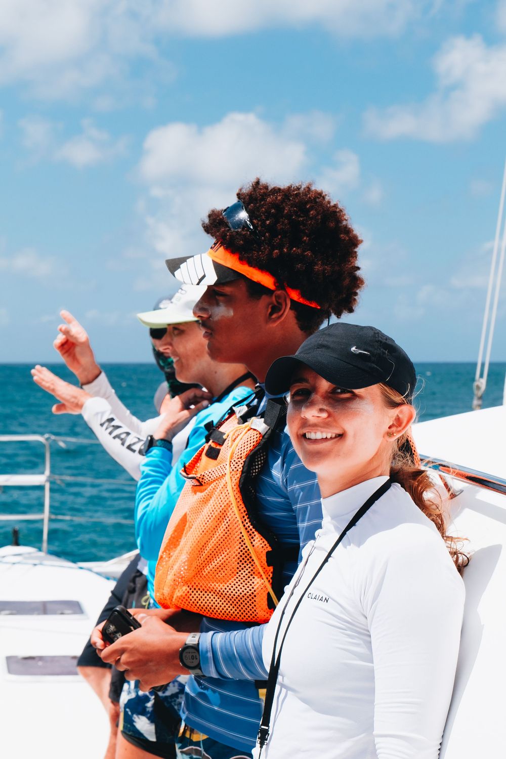A group of people enjoy a sunny day on a boat deck with bright blue ocean waters and sky in the background.