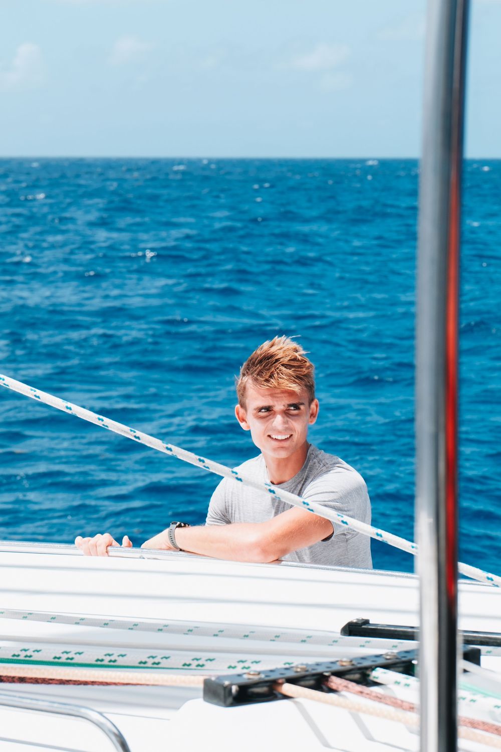 Someone relaxes on a sailboat deck against a bright blue ocean background on a sunny day.