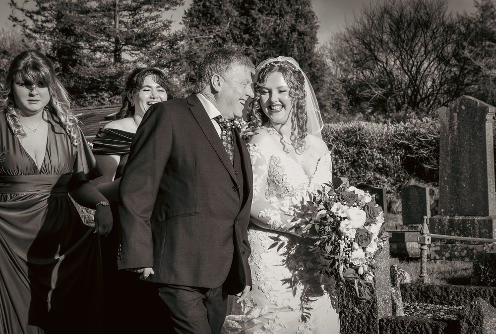 A black and white wedding photo in an outdoor garden setting with a bridal party holding a cascading bouquet.