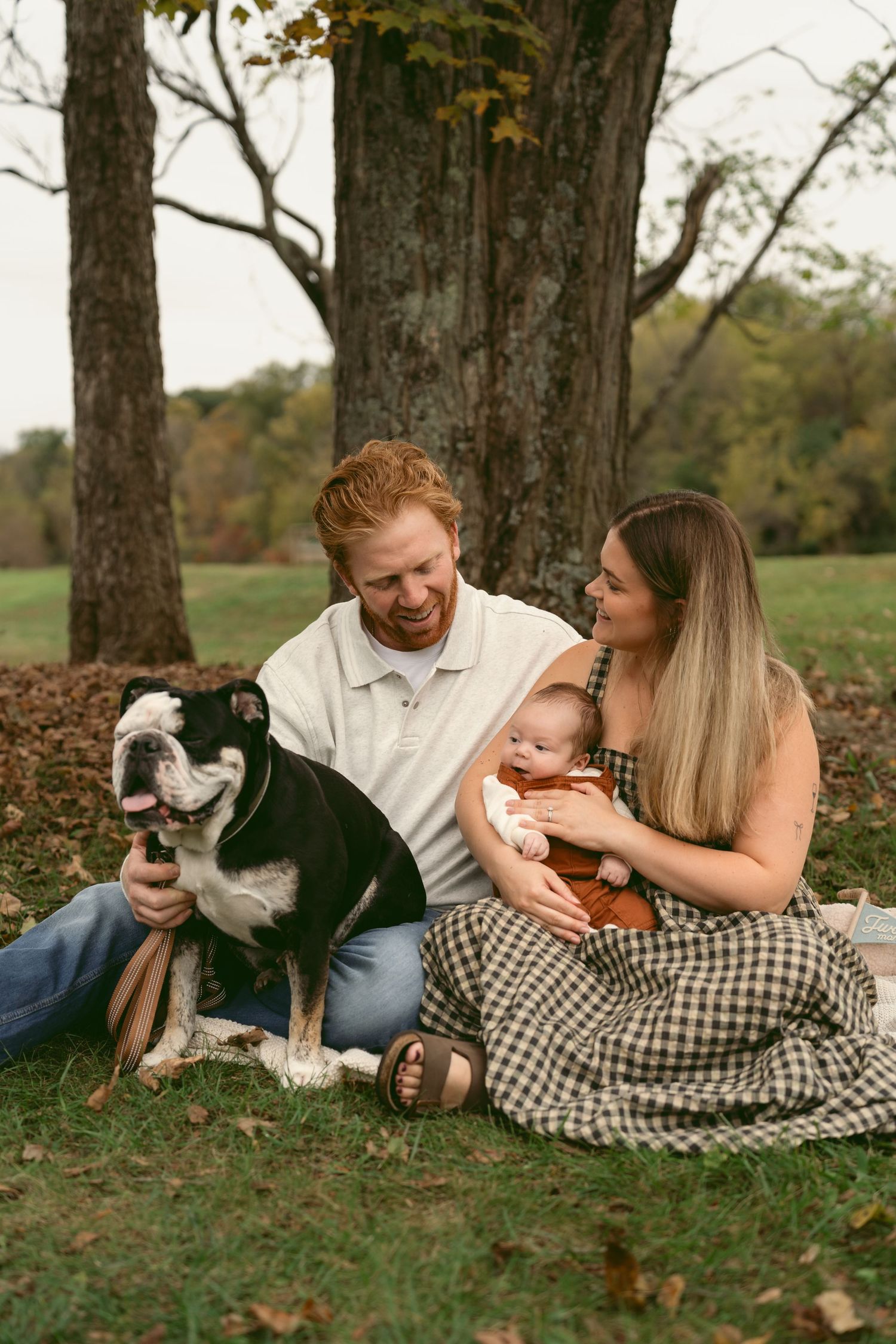 A family relaxes on autumn grass with their black and white dog during an outdoor photo session in Bellbrook Ohio.