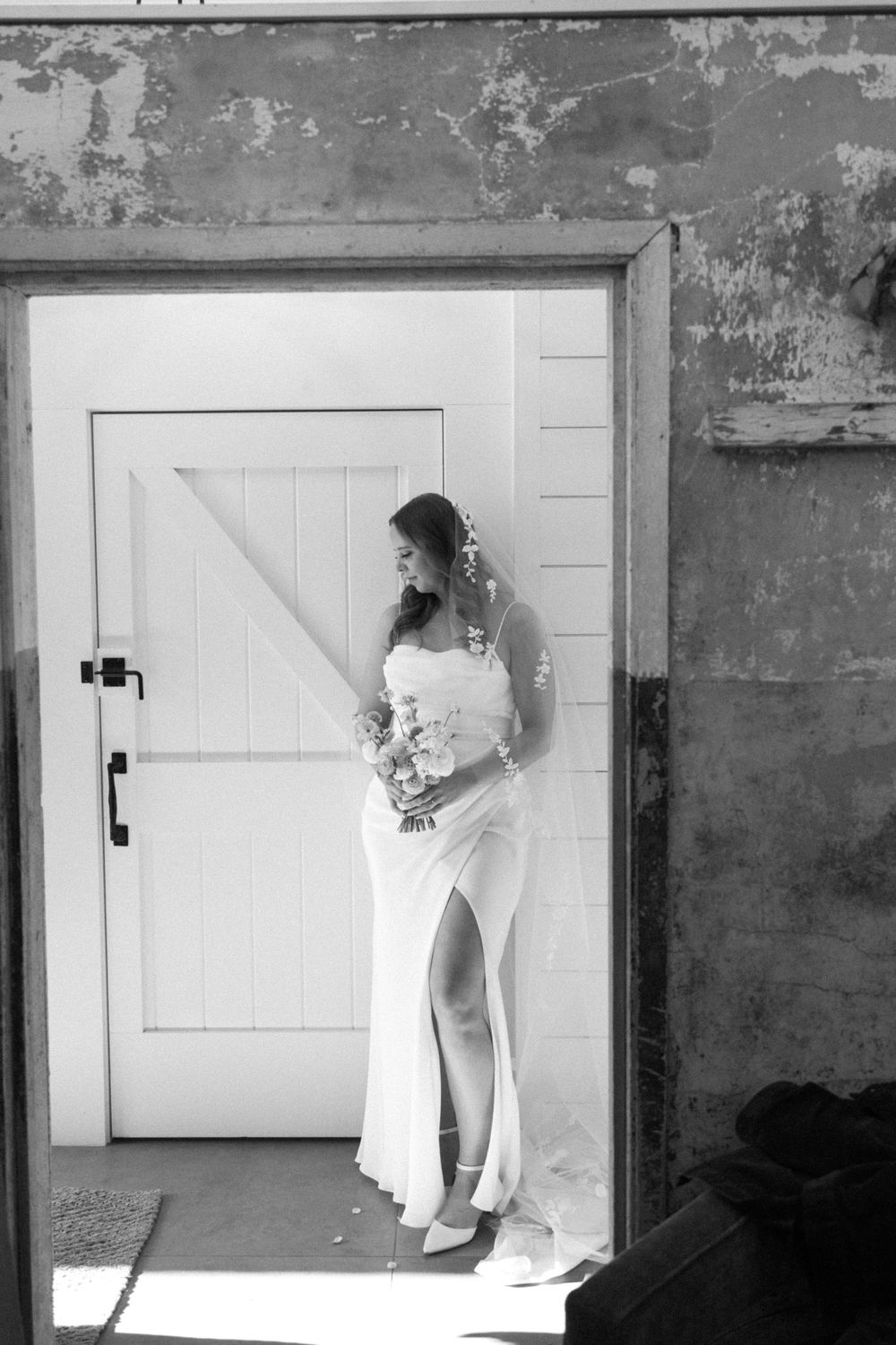 Black and white portrait of bride holding bouquet in doorway with dramatic lighting.
