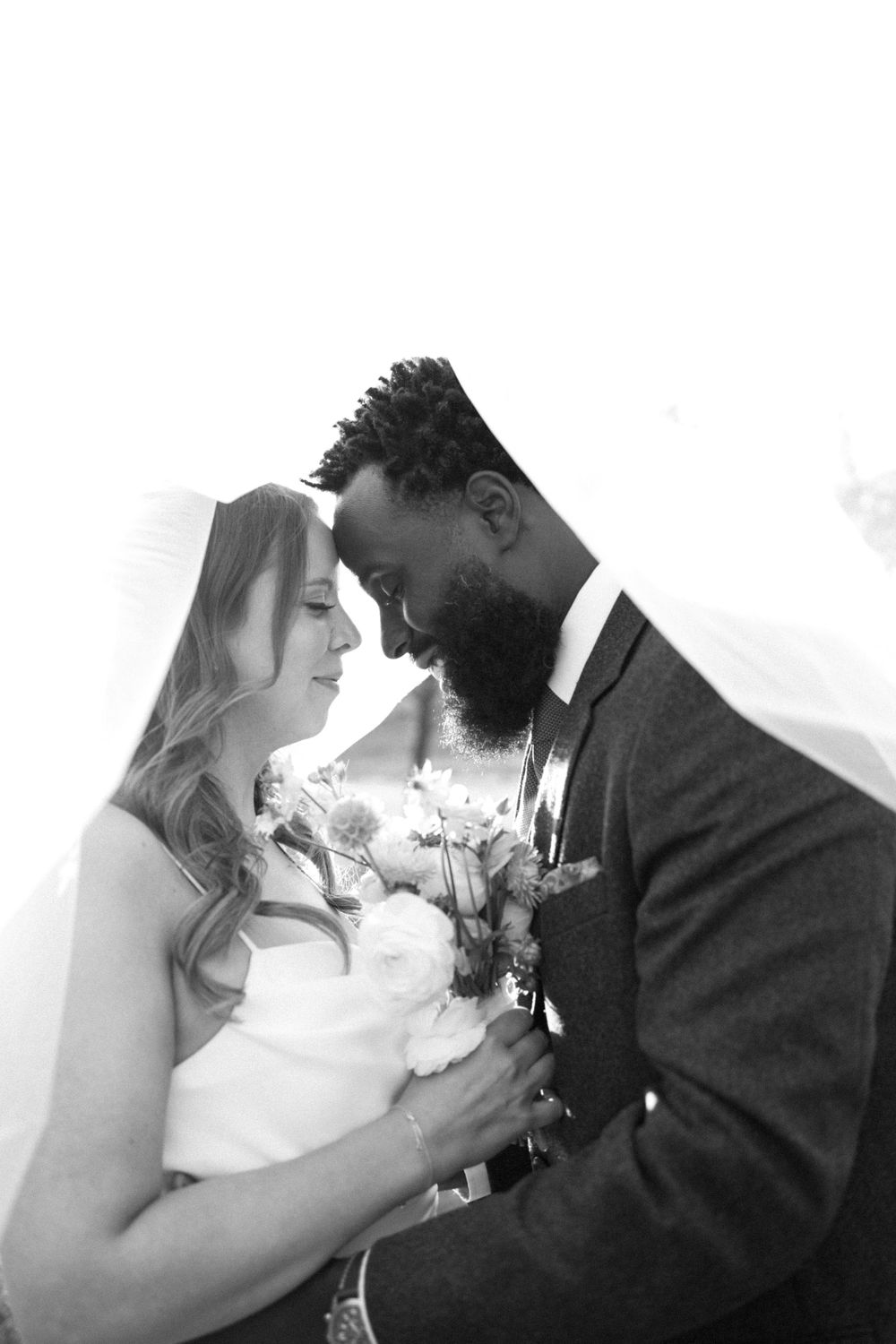 Black and white portrait of newlyweds sharing romantic moment with bouquet.
