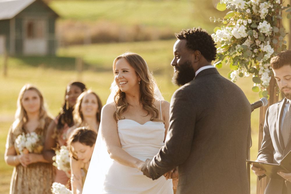 Joyful wedding ceremony takes place in a sun-drenched field with autumn colors in the background.