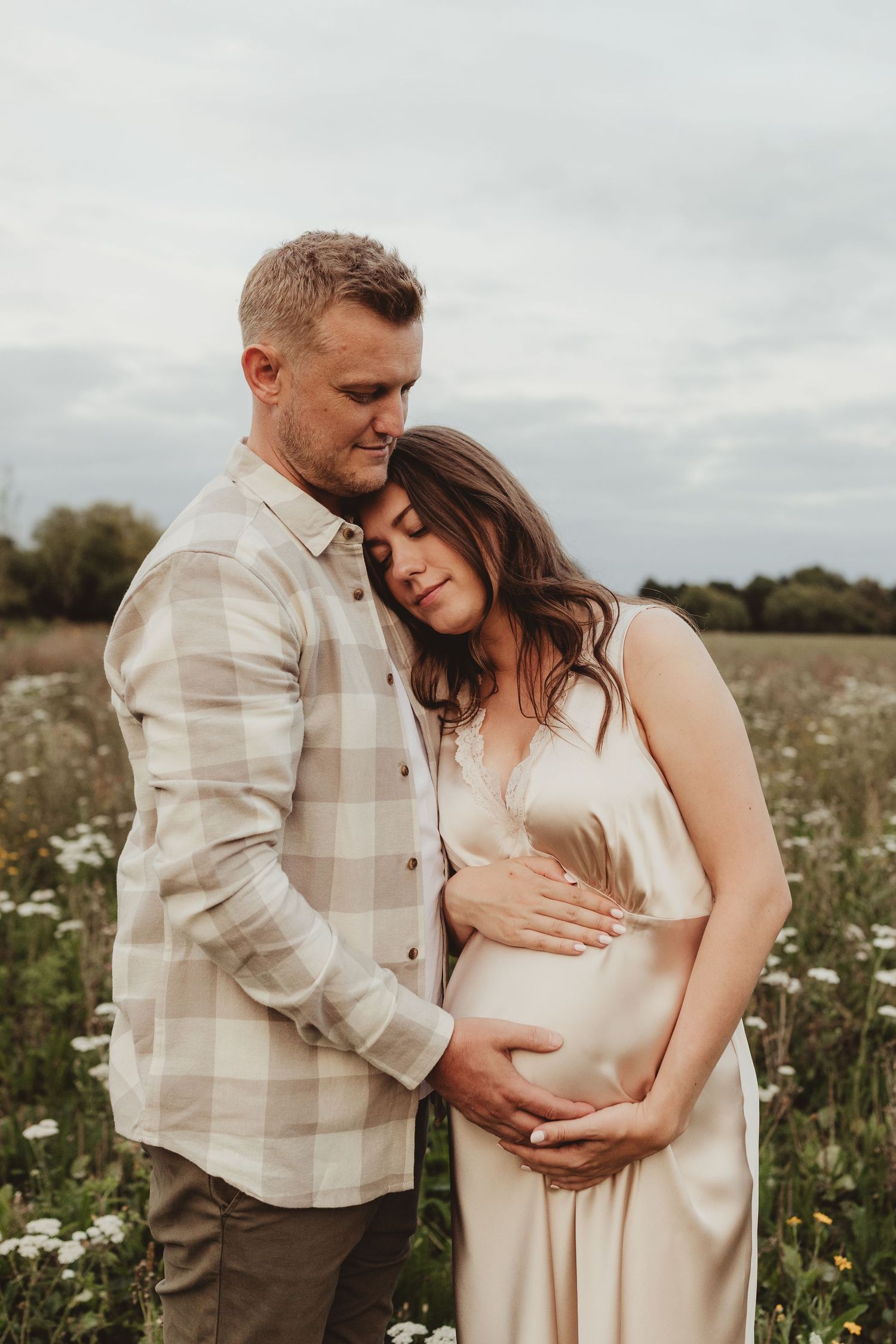 Expectant mother in yellow floral dress laughs joyfully while standing in a field of wildflowers.