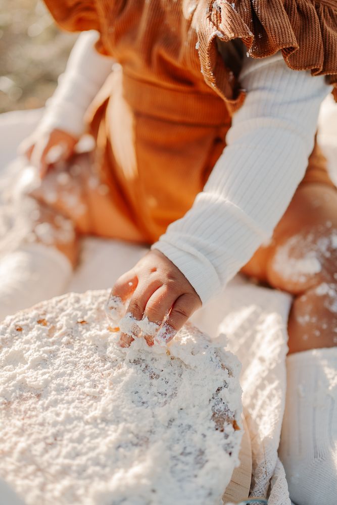Nahaufnahmen zeigen kleine Hände, die während einer sonnigen Fotosession im Freien mit weißem Zuckerguss spielen.
