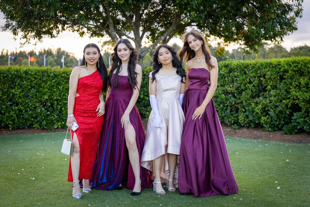 Sydney Event Photography - Four people in formal attire posing together on a green lawn with hedges in the background.