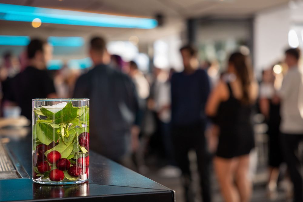 Sydney Event Photography - Cocktail with fresh fruit and herbs sits on bar counter at crowded social event.